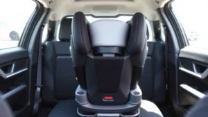 Professional photograph of a properly installed rear-facing infant car seat in a vehicle back seat, showing correct positioning and harness adjustment, with natural lighting from vehicle windows