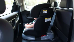 Professional photograph of a correctly installed rear-facing infant car seat in a vehicle's back seat, showing proper harness positioning and recline angle, shot from the side angle to clearly display installation details, natural lighting through car windows